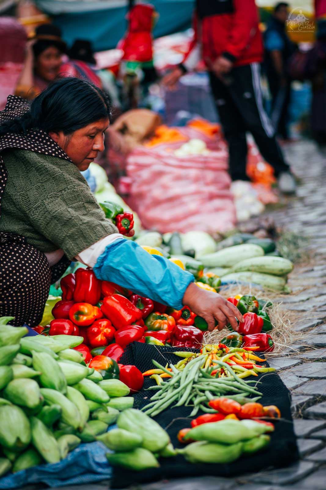 A woman reaches for peppers on a cobblestone street market in La Paz Bolivia.